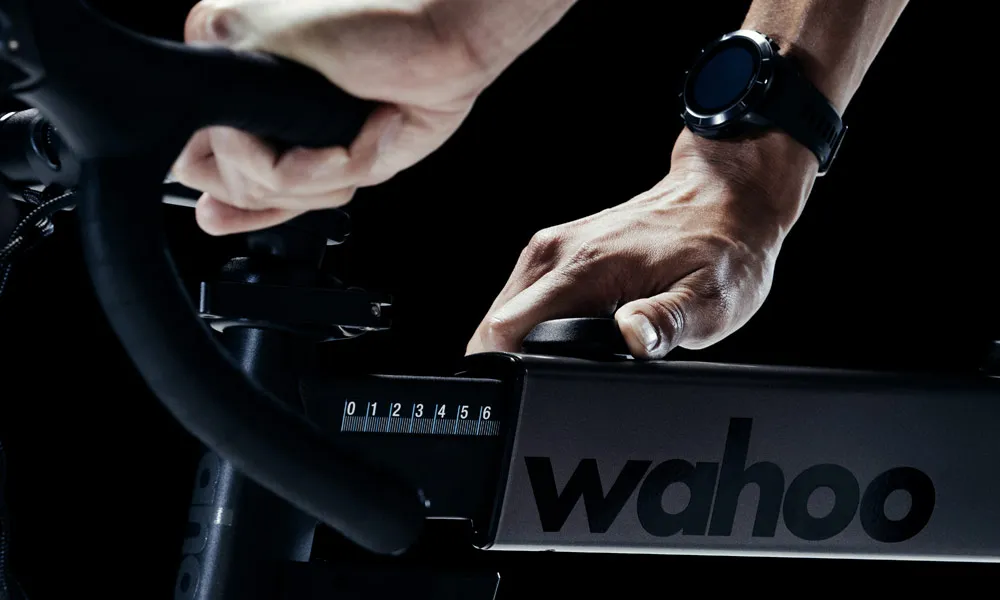 A cyclist wearing a Wahoo watch and adjusting the reach of a Wahoo Smart Bike