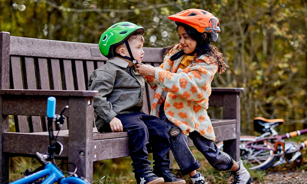 Child helping another child put on a bike helmet