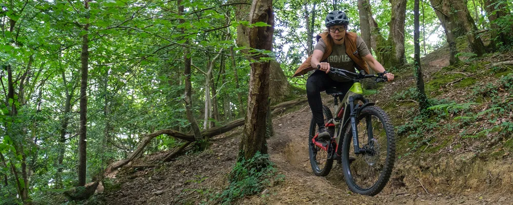 Woman riding steep MTB trail in the woods on a Cannondale Moterra eMTB wearing Troy Lee Designs cycling kit