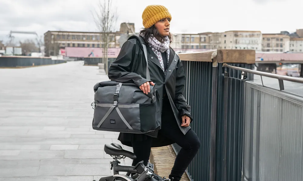 woman with brompton standing next to a railing with a messenger bag