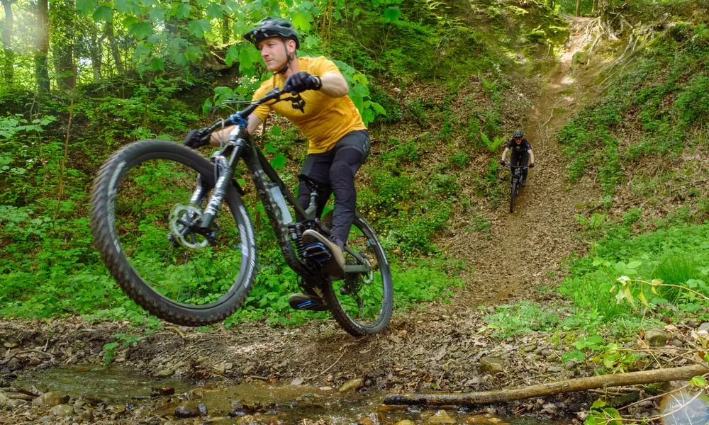 Mountain bikers riding down chute and over a stream in the woods