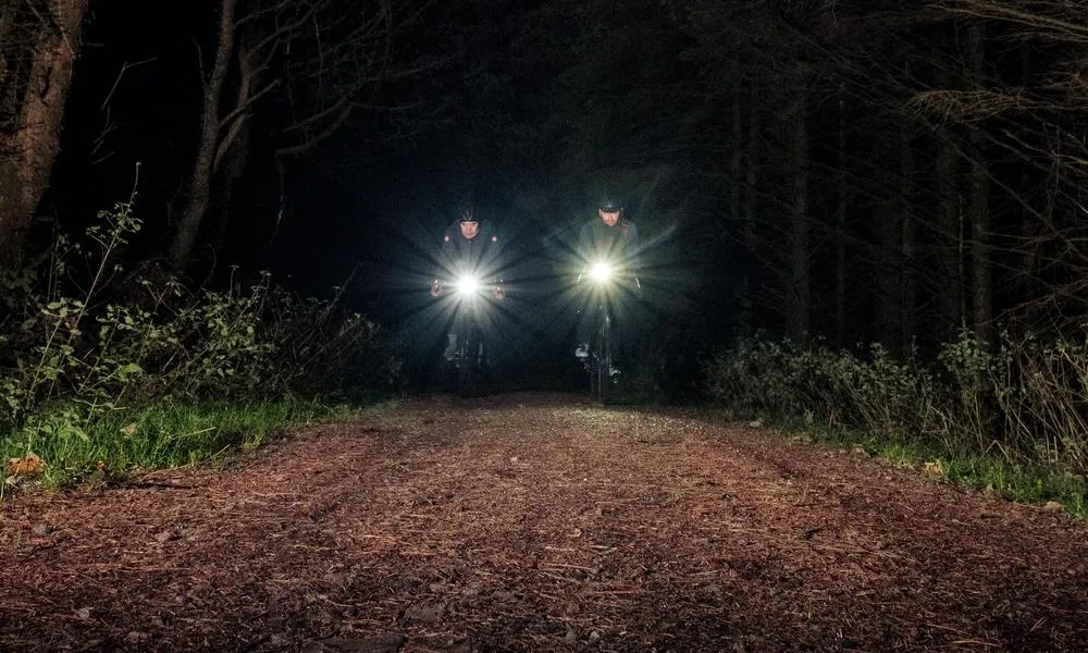 two riders cycling on a gravel road at night with lights