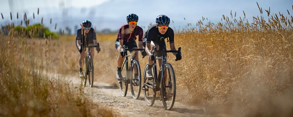 Three women ride cyclocross bikes through a field