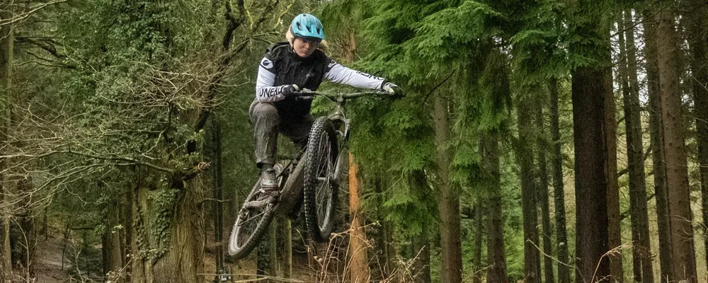 woman jumping an e-bike in the woods on a wet winter day