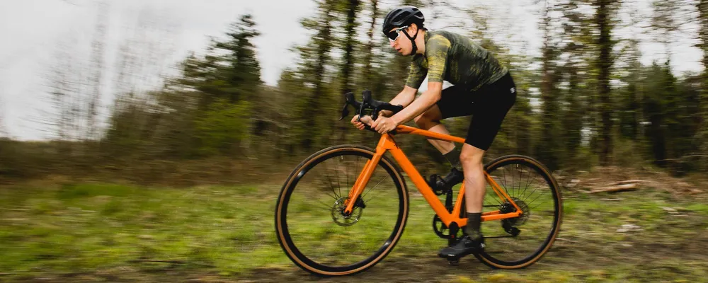 Gravel cyclist riding an orange gravel bike on rough terrain