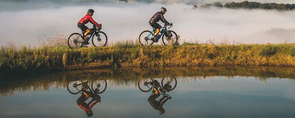 two cyclists on electric gravel bikes pass a mountain lake with cloud behind