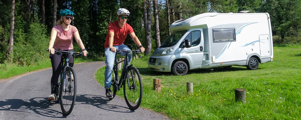 Hybrid bikes are ridden past a camper van