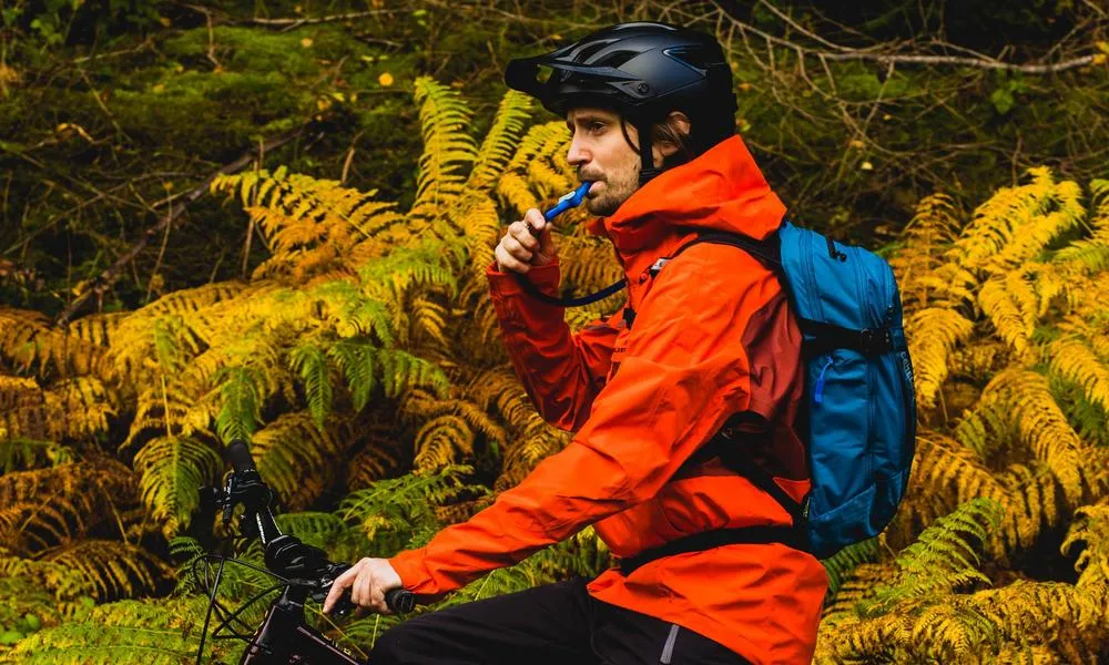 MTB rider in orange endura jacket drinking out of camelback