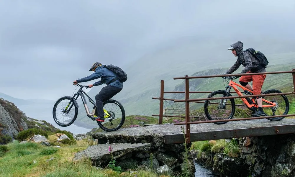 two electric mountain bike riders riding off a drop on a wet day in the mountains