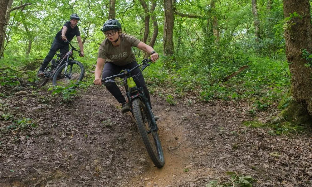 Two mountain bikers on Cannondale e-bikes riding in the woods on a warm summer day