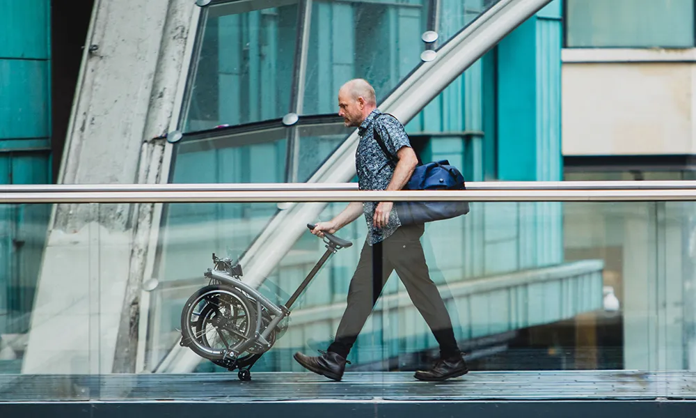 A folding brompton bike is pushed across a bridge