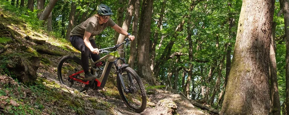 Woman riding a Cannondale Moterra electric mountain bike in the woods on a sunny summer day