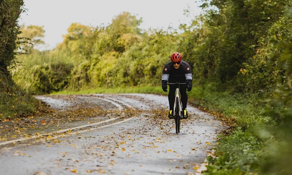 Road rider cycling among leaves and wet road