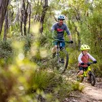 A young cyclist and his dad riding along a forest trail