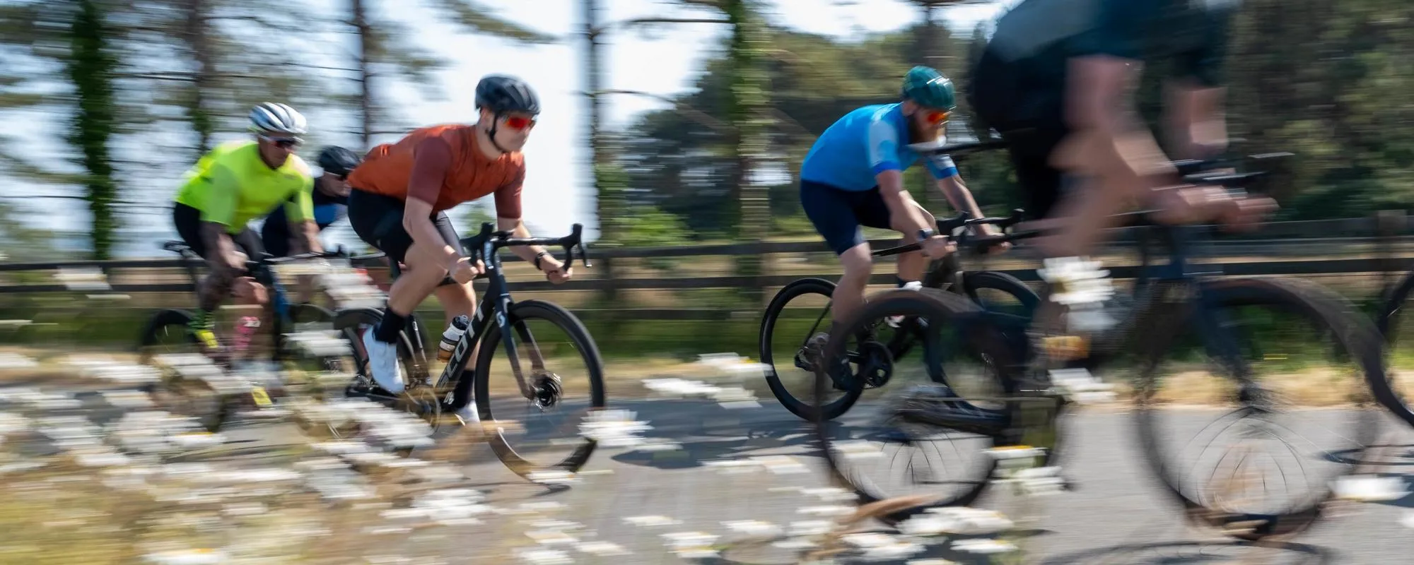 pan shot of road cyclists riding in a bunch past some flowers