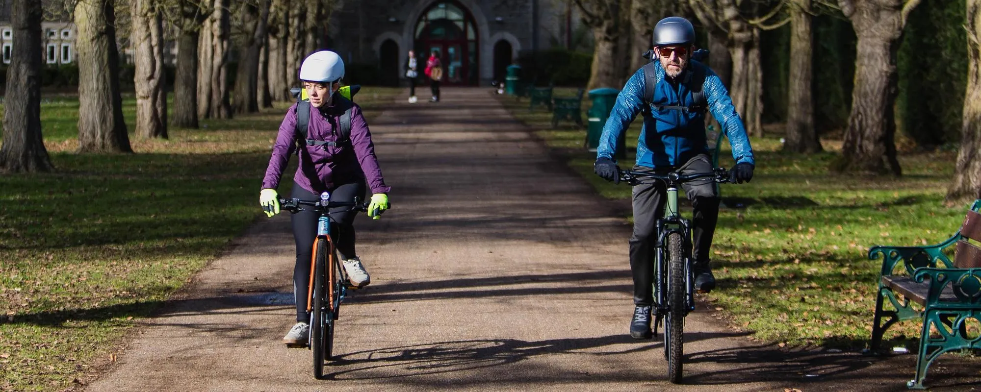 two cyclists riding side by side along a straight road in an urban park