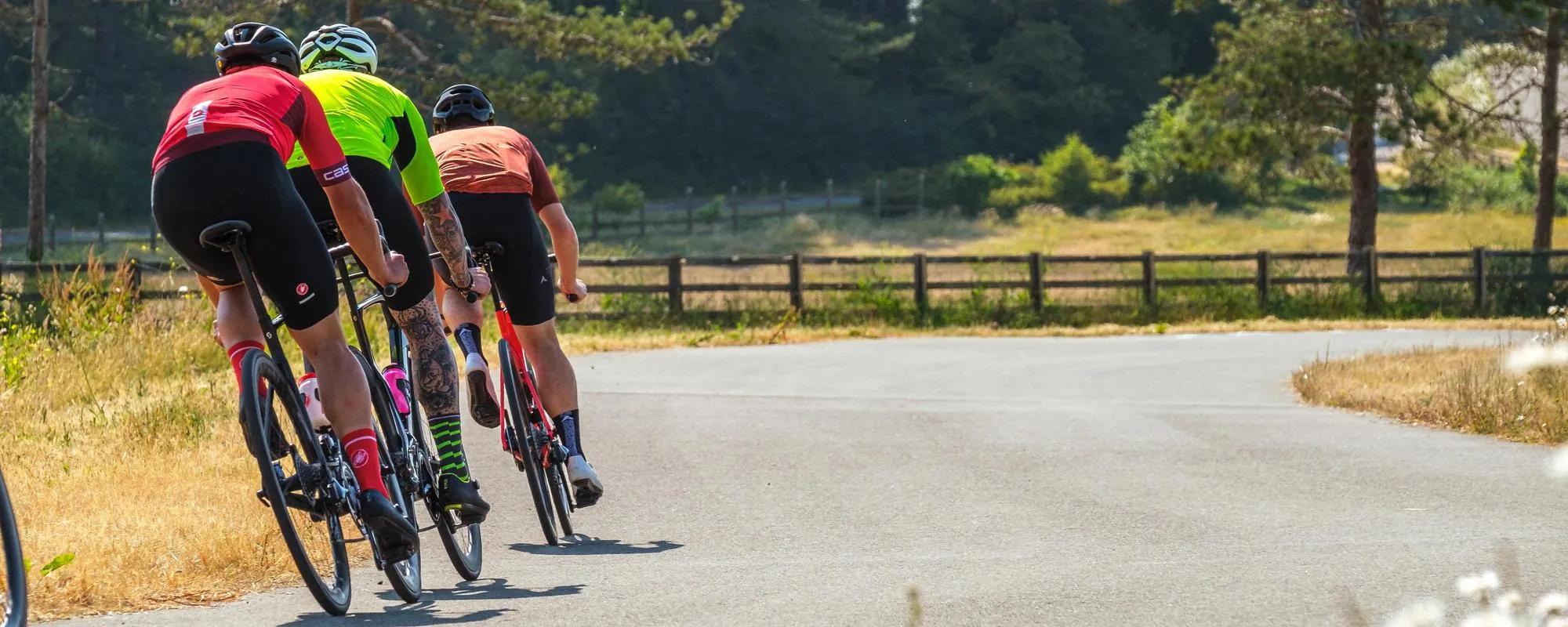 Three road cyclists approaching a corner on a sunny day on the countryside