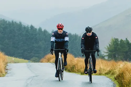 Two road cyclists riding on an open road in the welsh hills on a cool autumn day