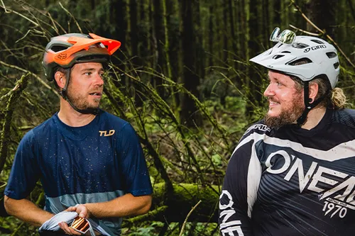 two mountain bikers with helmets on share a joke