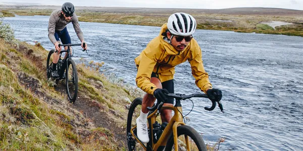 Gravel cyclists riding along a narrow trail next to a lake