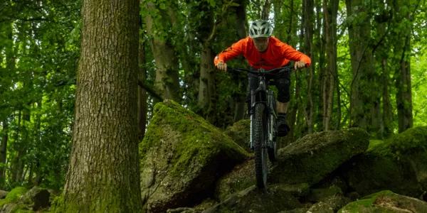 A mountain biker riding a Merida full suspension bike through a forest trail