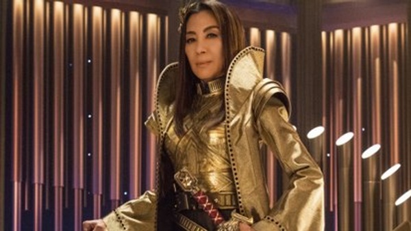 Picture of woman wearing a golden outfit with shoulder pads and a dramatic high collar