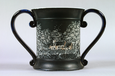 Photograph: Early twenteith century Benthall Pottery Co. two-handled mug or loving cup decorated in black slip, with sgraffito work Benthall scenes (church and Benthall Hall). Dated to c.1900-1920.