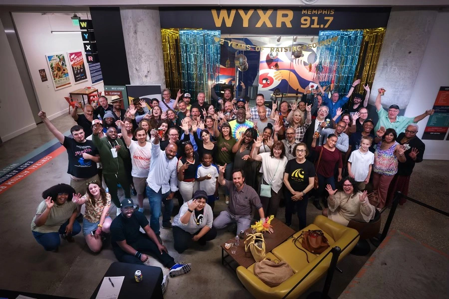 Overhead group shot of 20-30 WYXR volunteers inside the Crosstown Concourse, waving at the camera. 