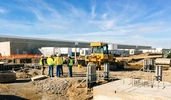 Crew of construction workers wearing high visibility vests and talking at a job site with tractors in the background