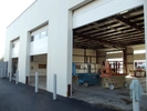 Outside of metal shop building with 3 roll up door open. You can see 2 scissor lifts and some stacked boxes inside. 