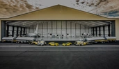 Large aircraft hangar filled with planes, trucks, and yellow sports cars