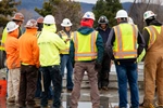 A large group of J.B. Steel, Inc. workers in hi-vis vests and hardhats having a safety meeting