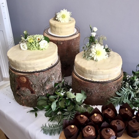 3 of Kernvoll's vegan wedding cakes covered in pale cream icing and presented on top of decorative logs with bouquets of flowers on top
