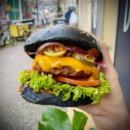 Someone holding a charcoal bun vegan burger whilst dining al fresco