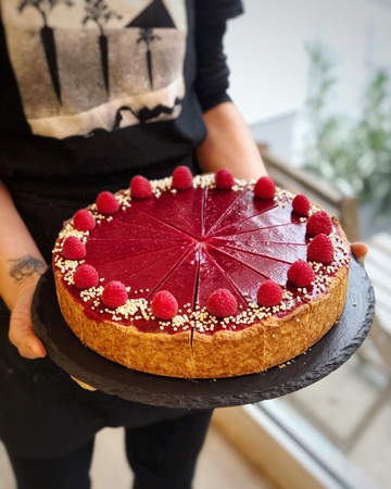 An employee from Berlin's vegan Plant Base holding a berry cheesecake with raspberries around the edges