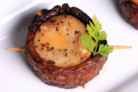 A plant-based scallop made from oyster mushroom and tempeh bacon, held together with a skewer. Photo credit: https://olivesfordinner.com/2012/10/vegan-bacon-wrapped-scallops-wi.html