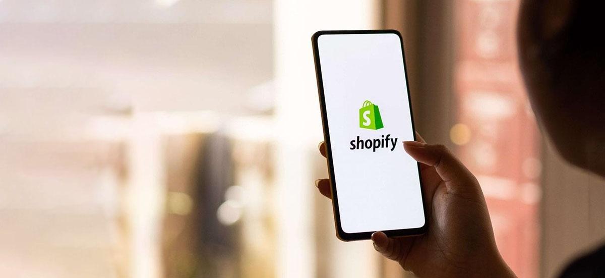 Eine Frau hält ein Smartphone mit dem Shopify Logo in den Händen