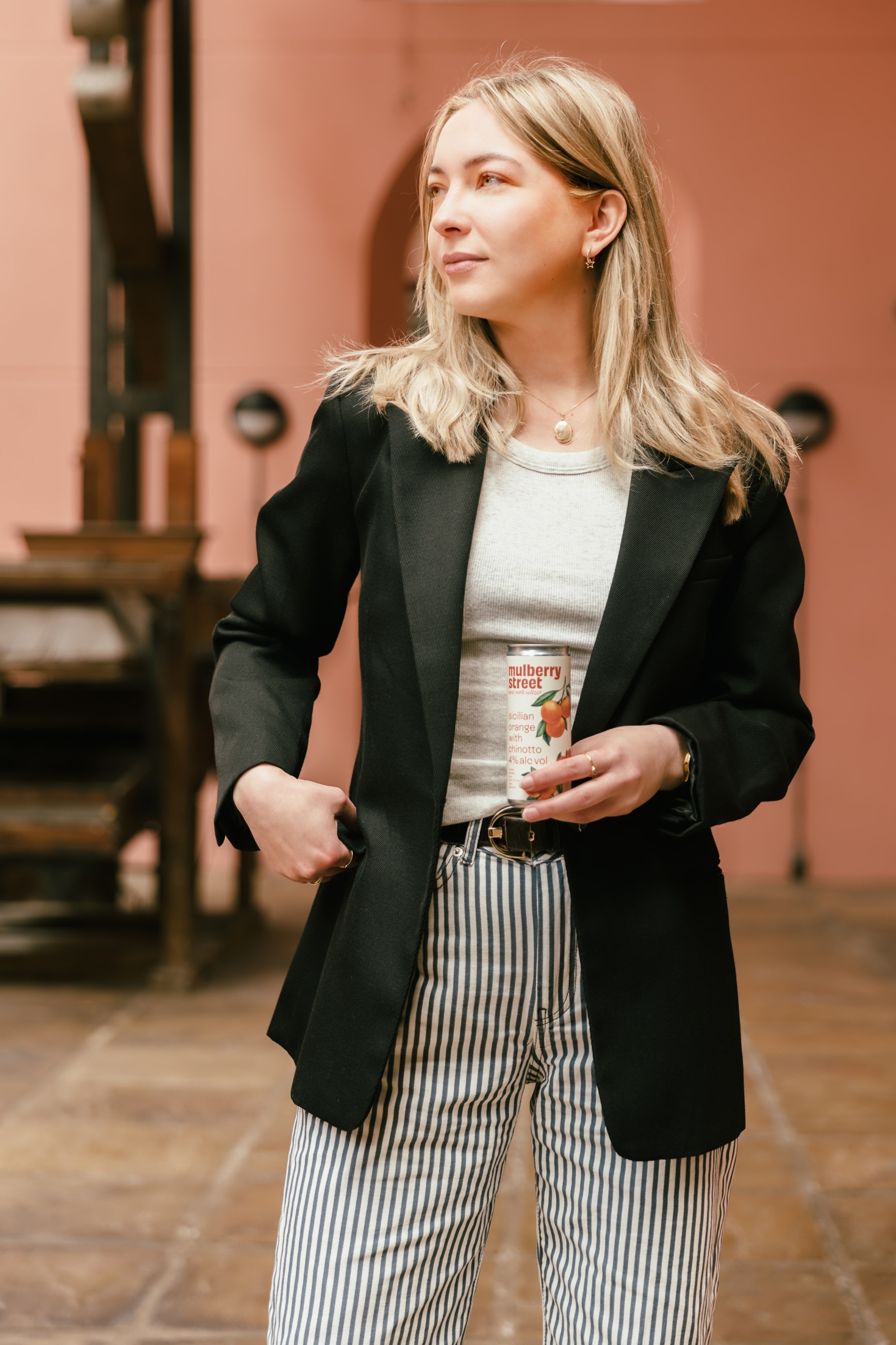 A person in a black jacket holding a can of Mulberry Street Orange Seltzer