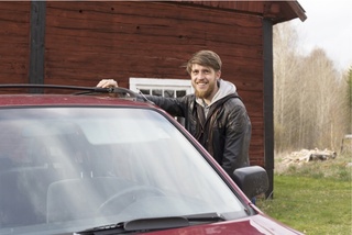 Smiling man standing behind a car