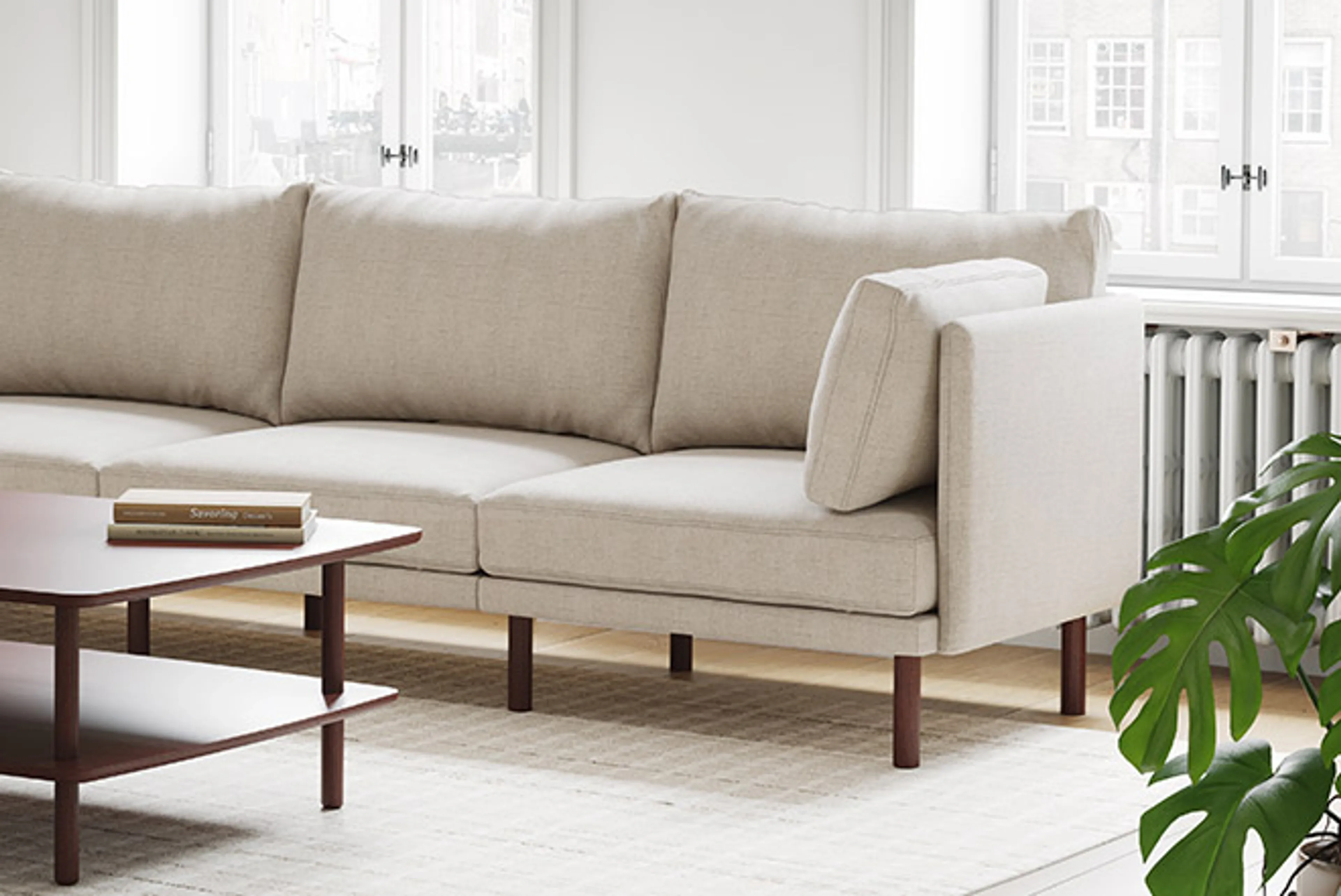 Field sofa in oatmeal with walnut legs shown in living room setting with rug and coffee table.