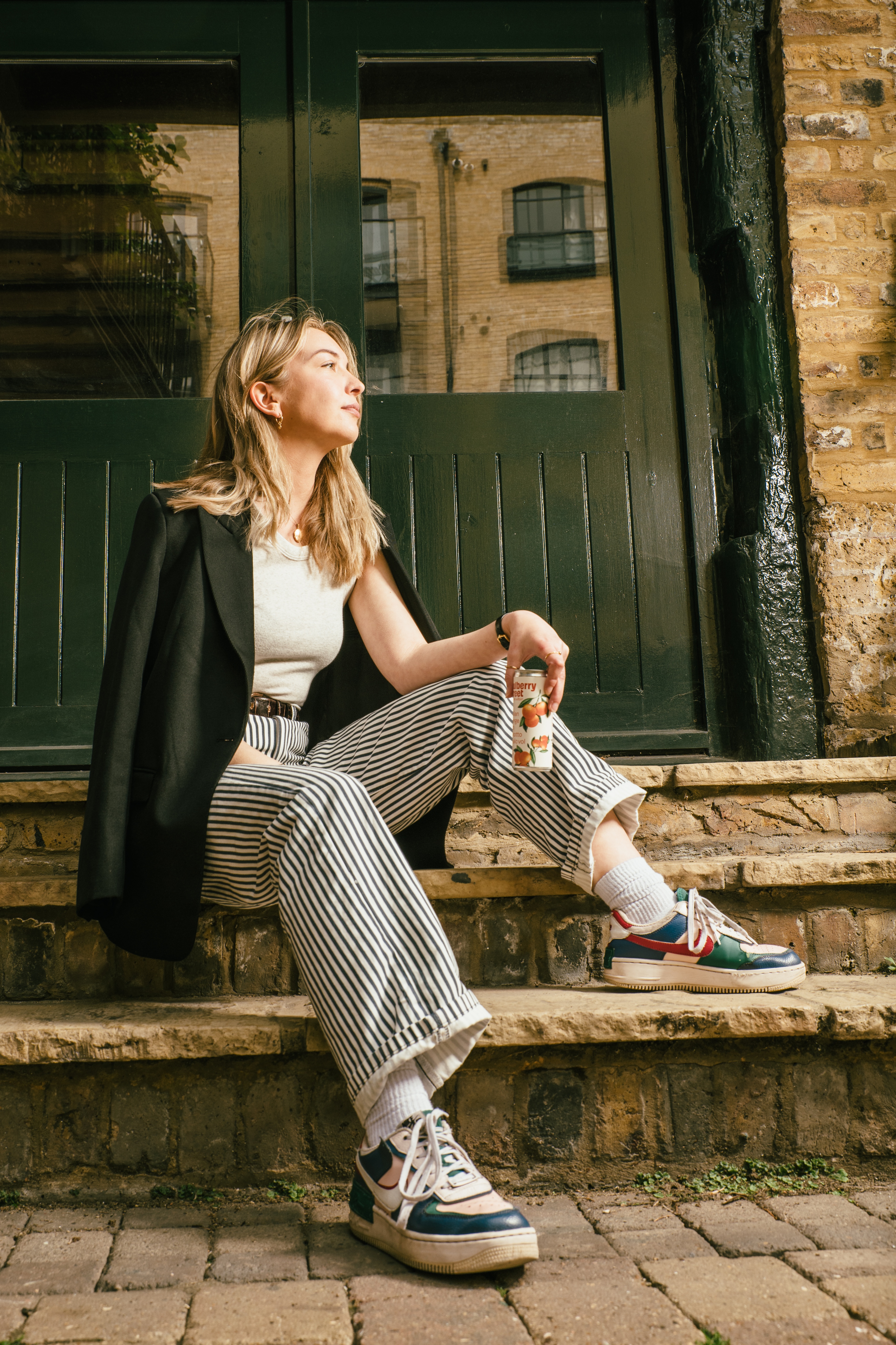 A person sitting on steps with a can of Mulberry Street Orange Seltzer