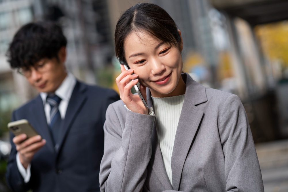 A businesswoman in a suit smiles while on the phone, possibly discussing a personal reference with team colleagues. 