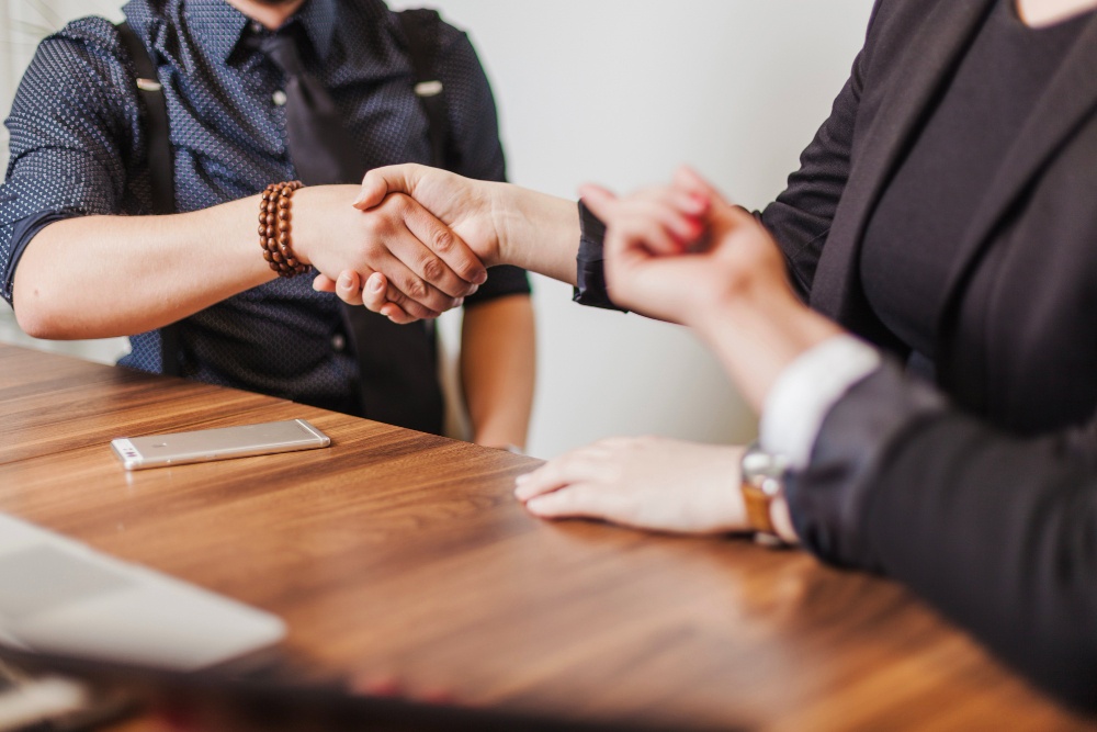 Two people shaking hands over a wooden table, illustrating effective communication and teamwork, key selection criteria examples for building strong professional relationships