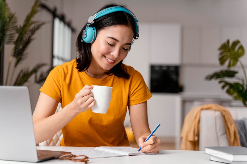 Seorang wanita sedang menulis sesuatu sambil menghirup minuman 