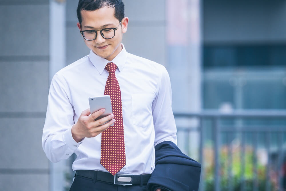 Seorang lelaki profesional sedang melihat telefon bimbitnya sambil berjalan. 