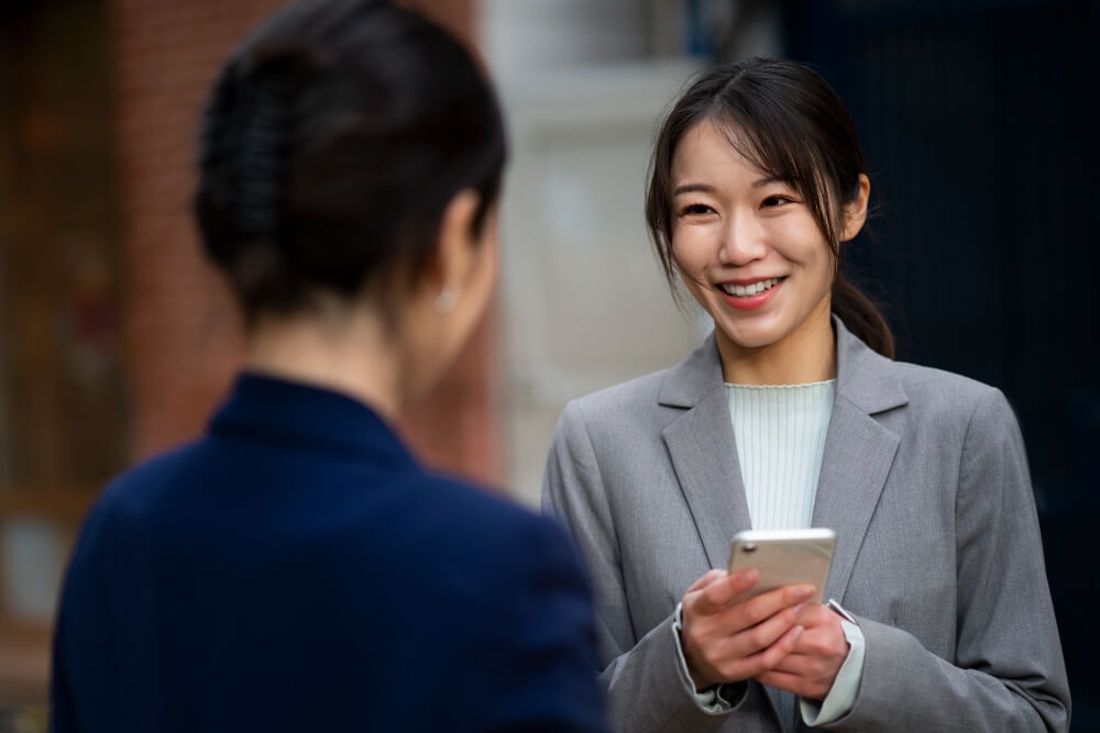 Seorang wanita tersenyum sambil memegang telefon bimbit dan berbual dengan rakan sekerjanya. 