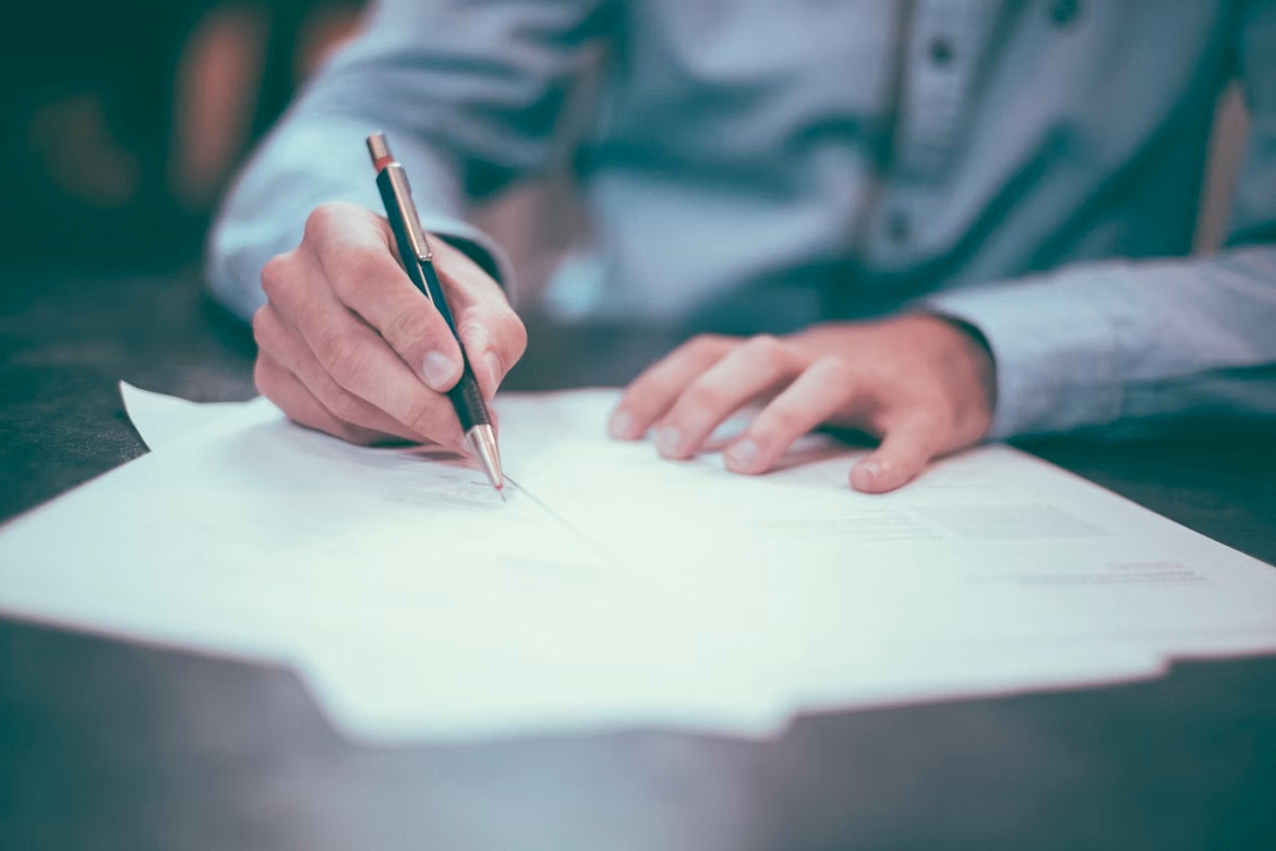 Man is writing something on a paper with a pen