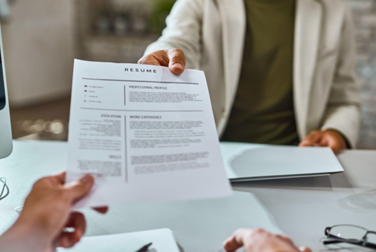 A job applicant hands over their resume during an interview, with selection criteria showcasing their qualifications and alignment with job requirements