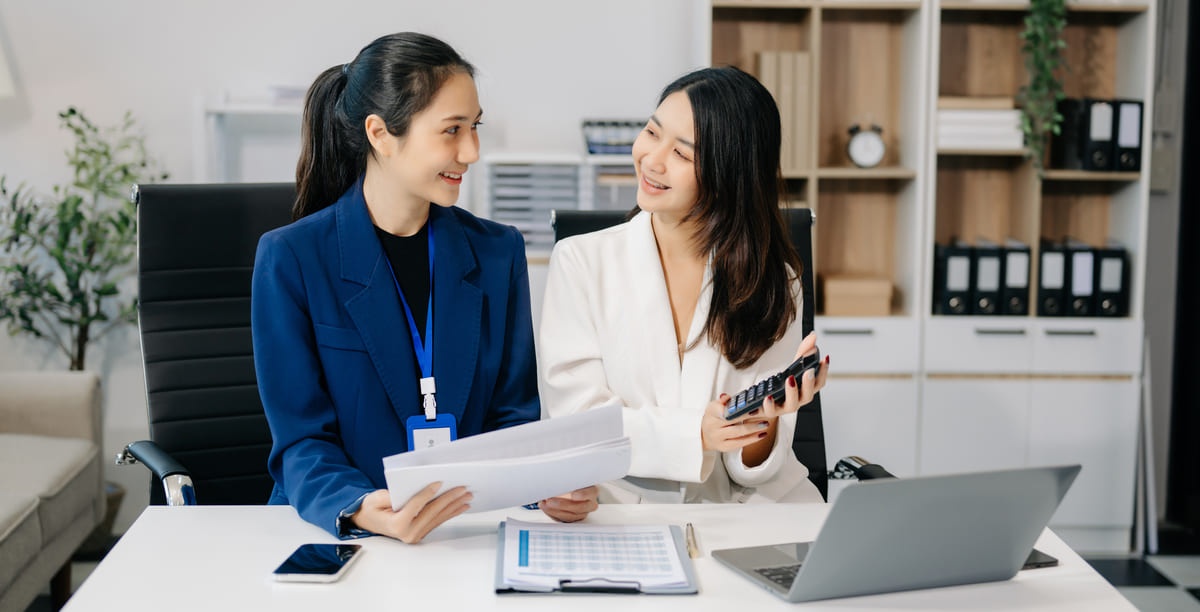 Dua orang karyawan wanita terlihat bahagia setelah selesai menghitung pajak natura di kantor. (Sumber: Envato)