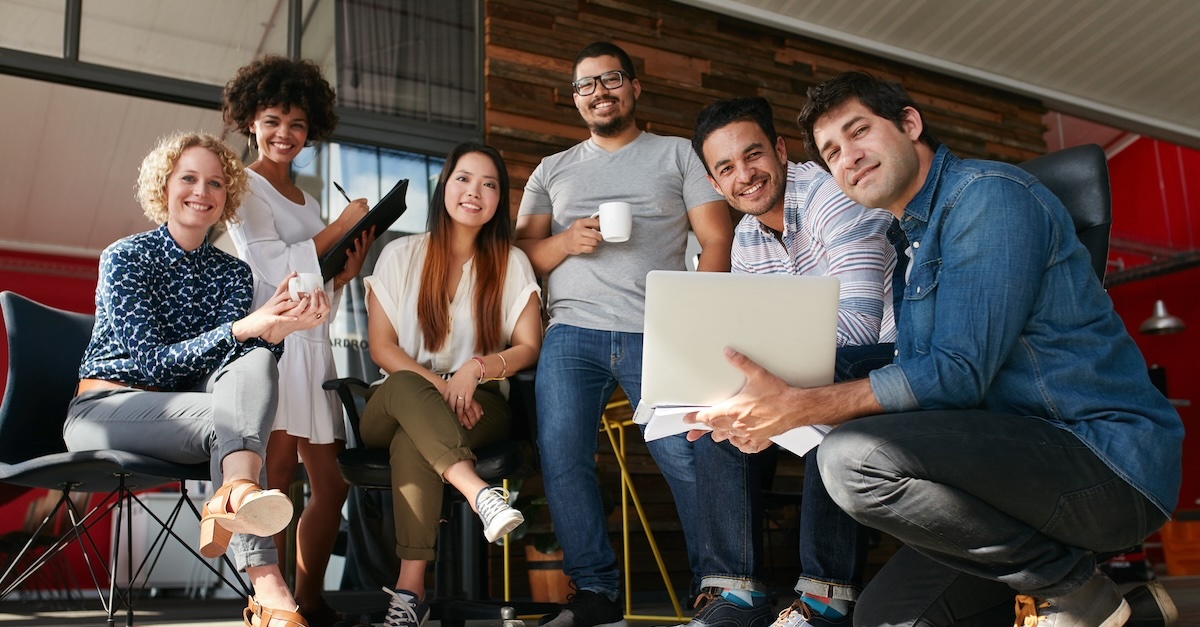 A relaxed  group of six, with cups and a laptop, brainstorm on office steps, reflecting a casual, creative workspace